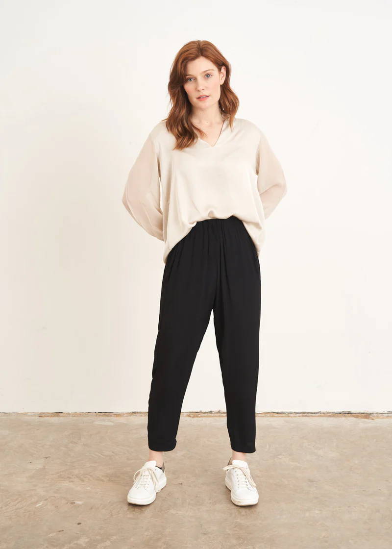 A model wearing an off white long sleeve blouse with black tapered trousers and white trainers 