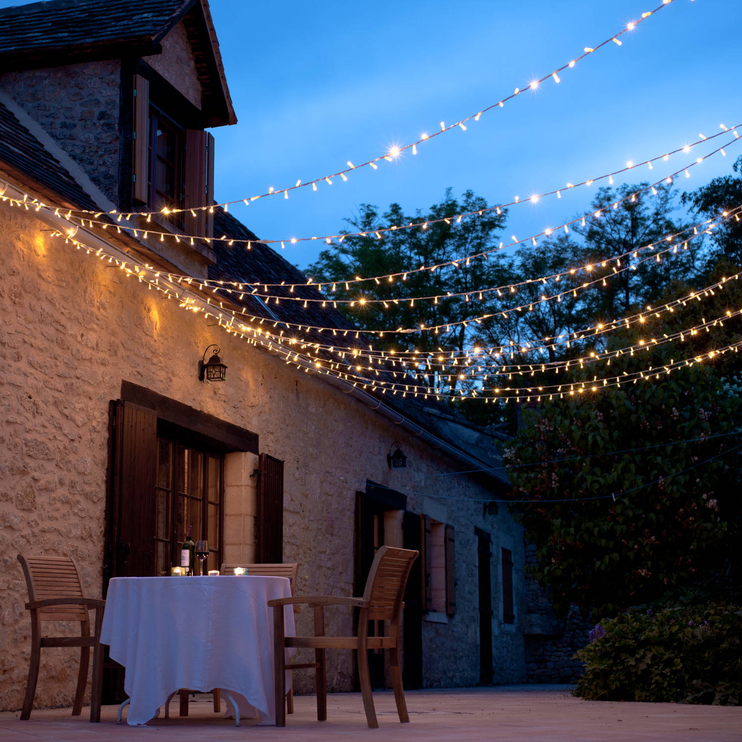 A warm white fairy light canopy above an alfresco dining setting 