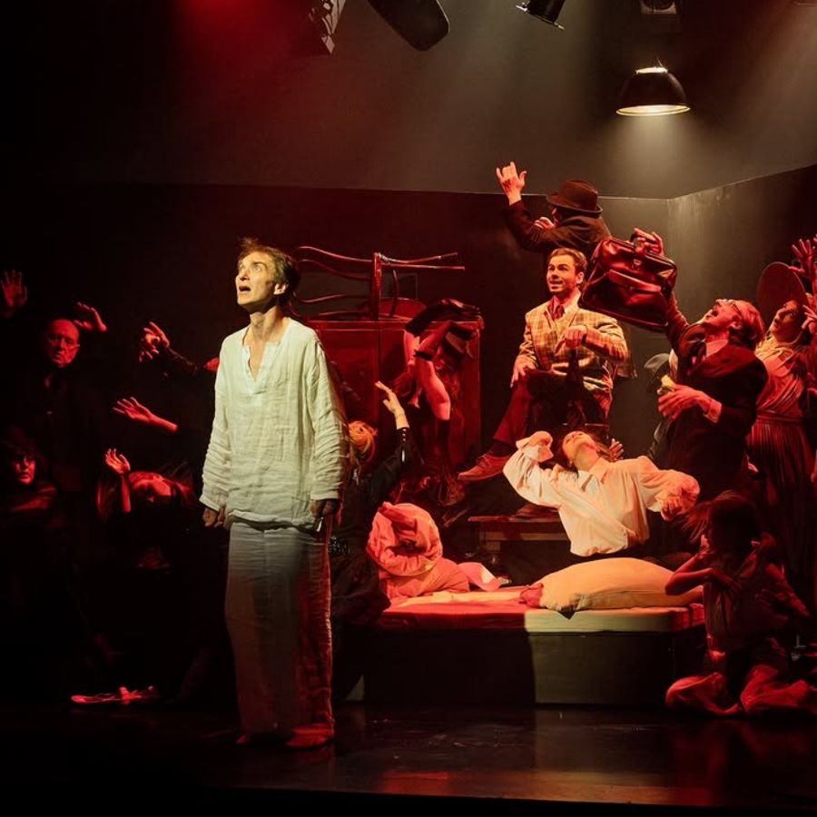 A dramatic theater performance with a central figure and ensemble cast.