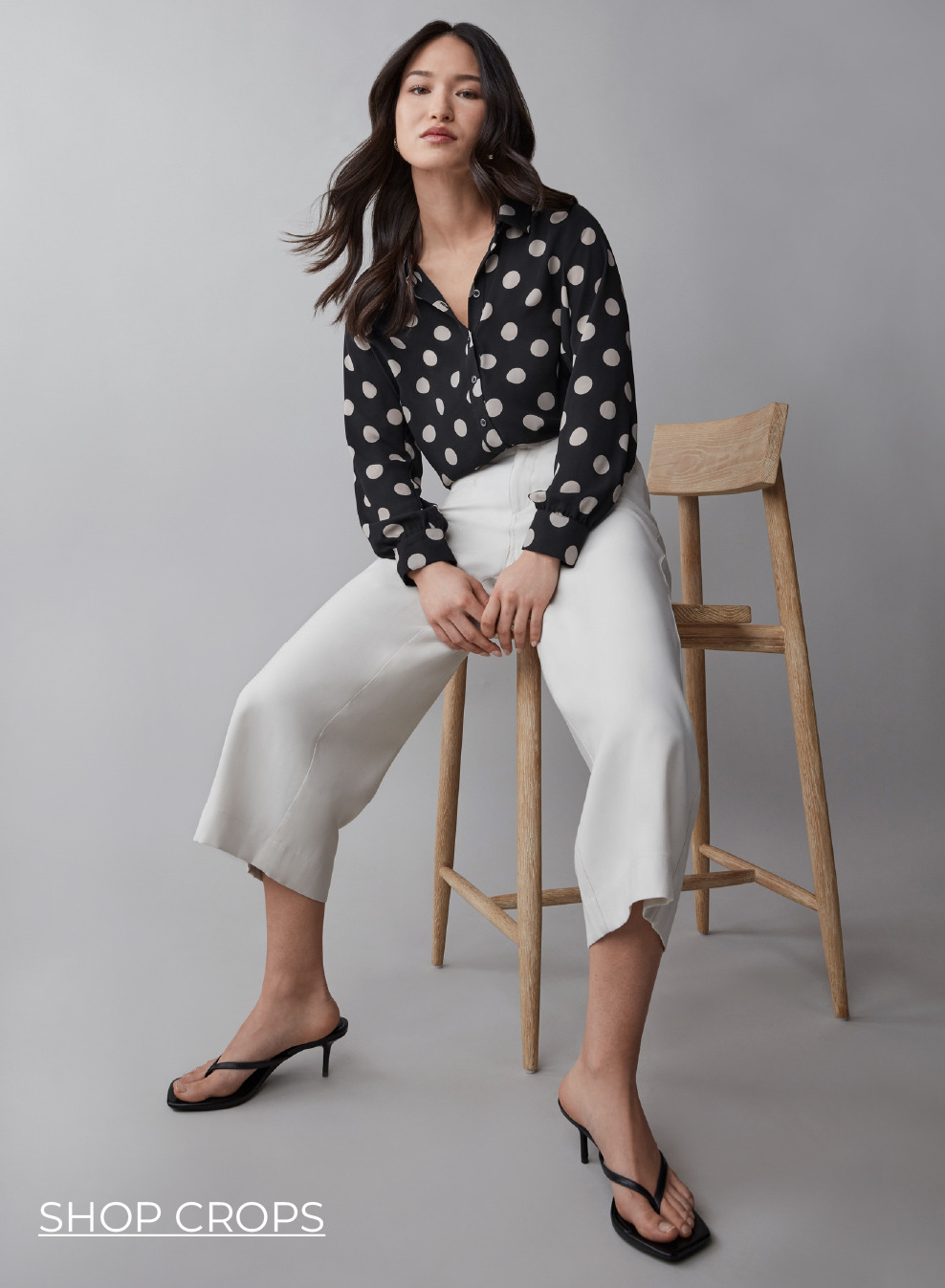 Woman sitting on a stool, wearing a floral shirt and white pants.