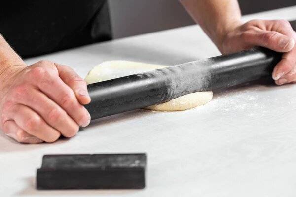 Dough is being rolled with a rolling pin on a floured kitchen surface.