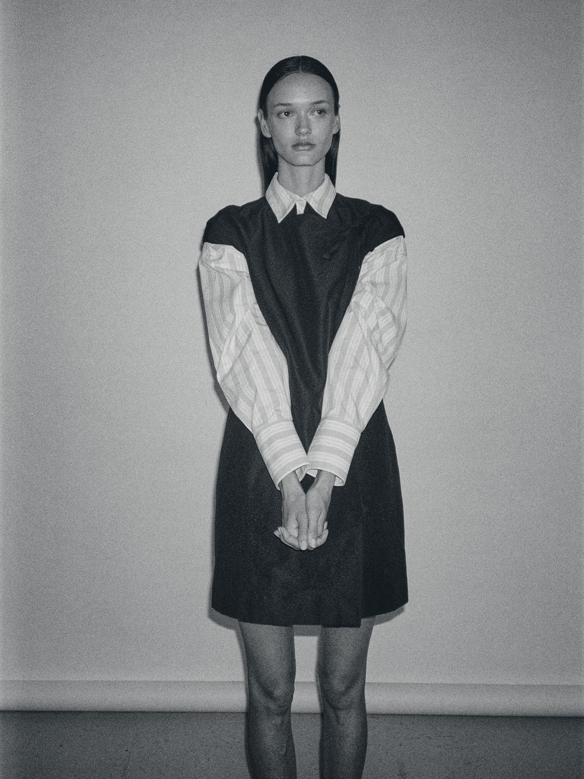 A person wearing a black dress with striped sleeves, standing against a plain wall.
