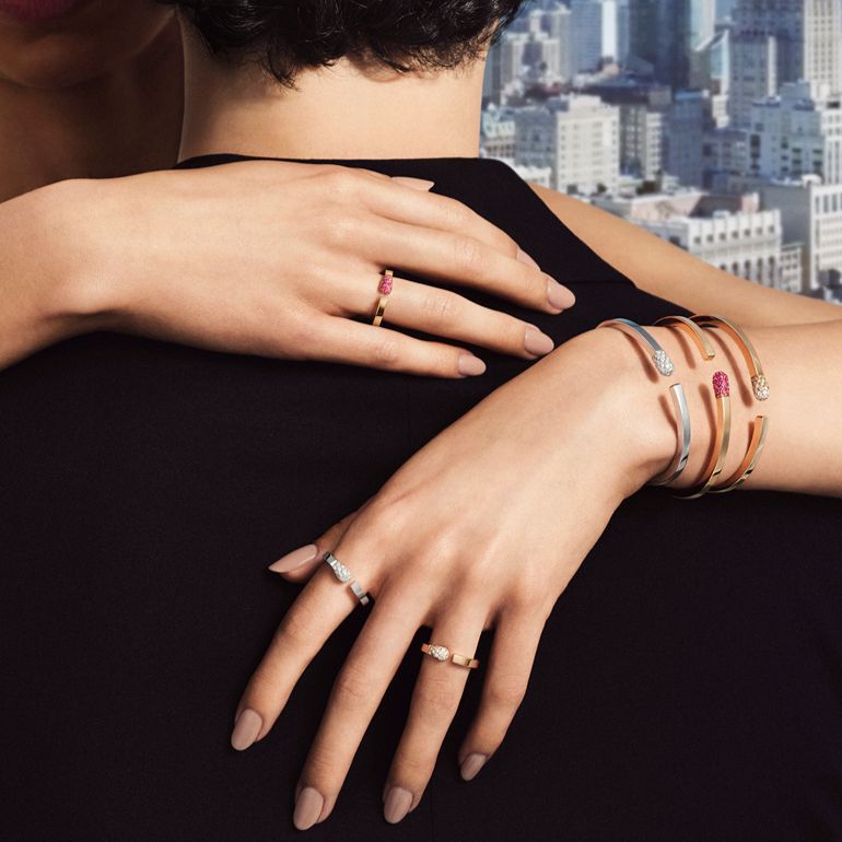 Hands adorned with jewelry resting on a person's shoulder against a city backdrop.