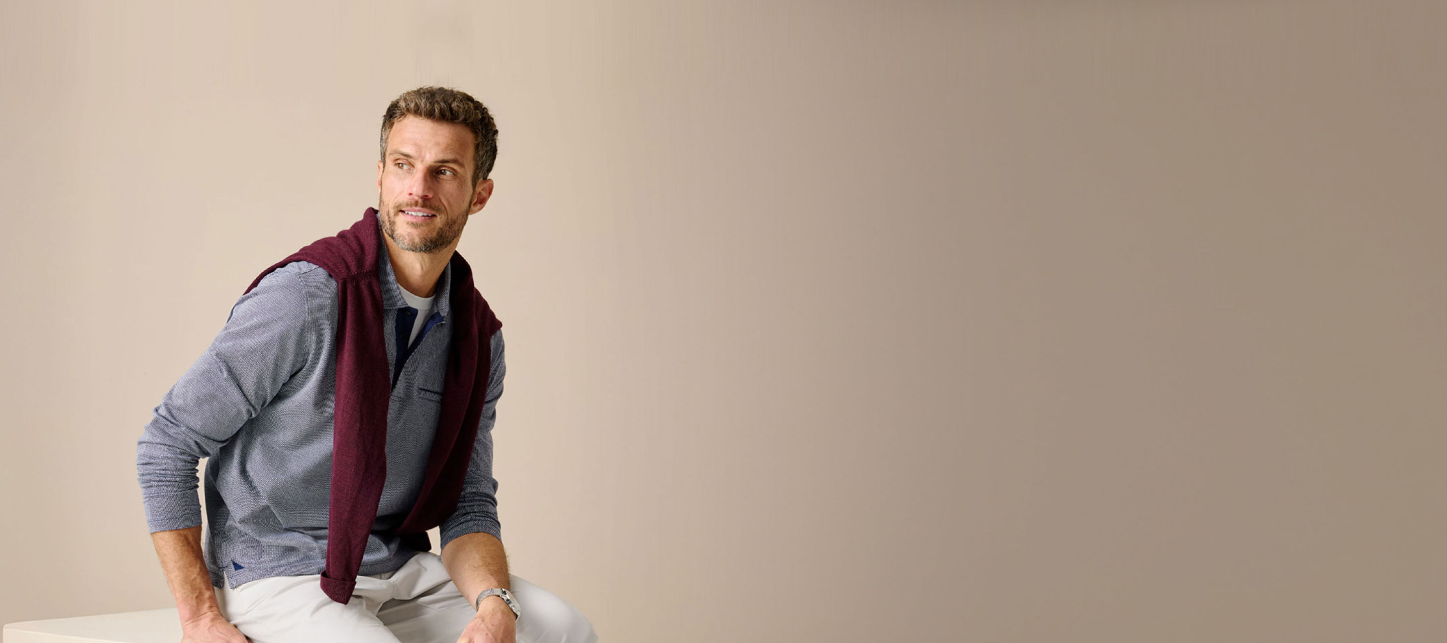 A man sitting casually, wearing a blue shirt and maroon sweater.