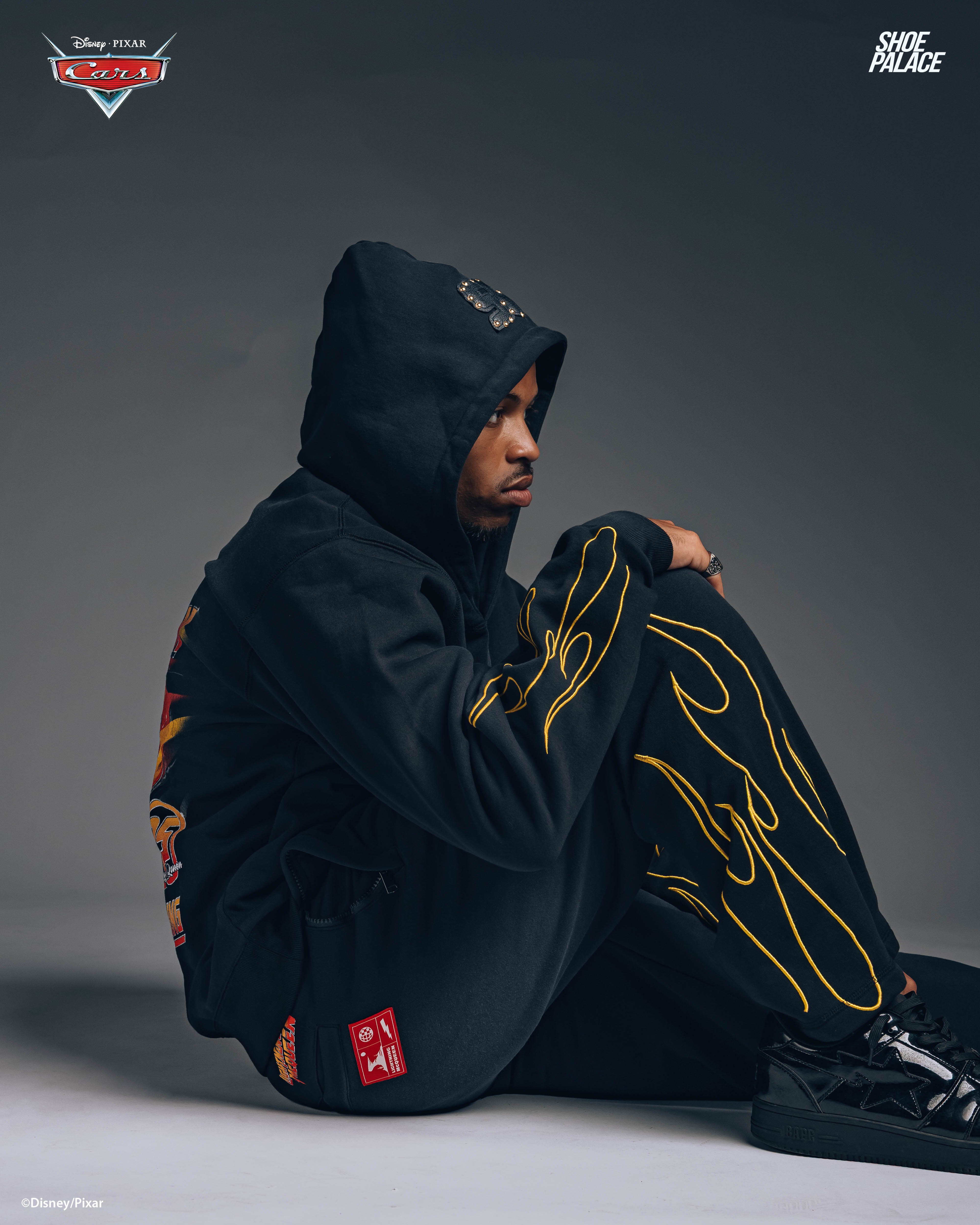 Person in hoodie and sweatpants sitting against a wall.