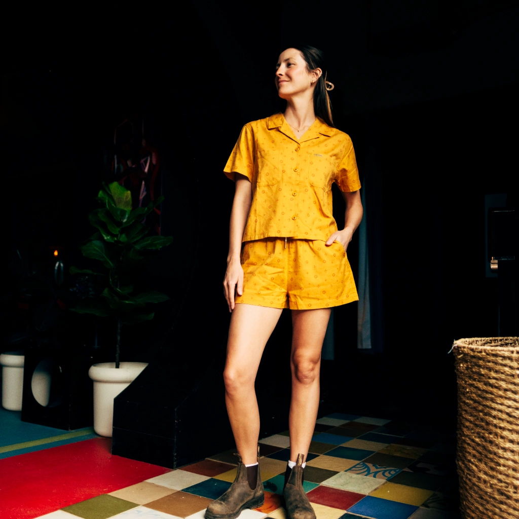 Person in yellow outfit standing on a colorful floor with a plant nearby.