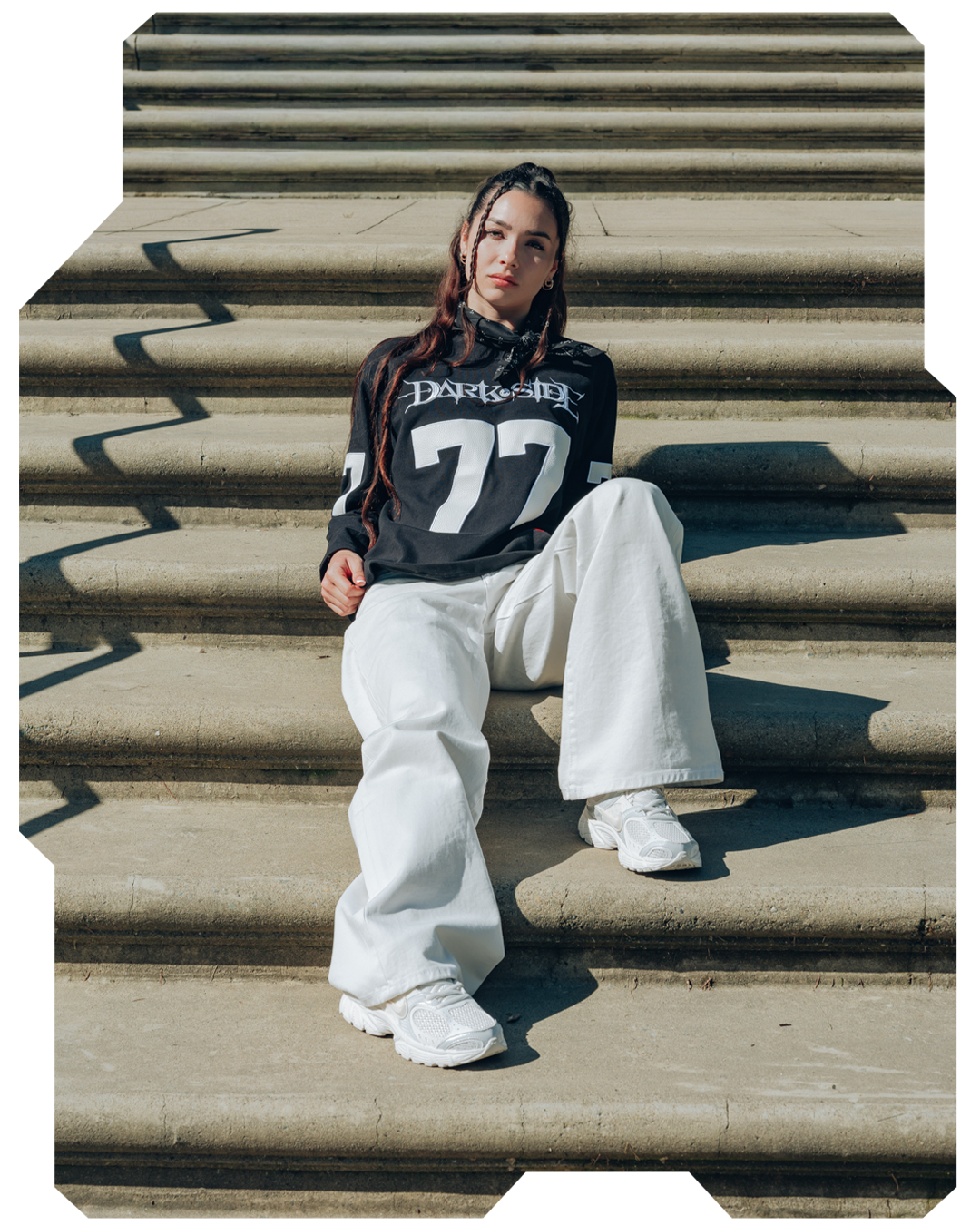 Young woman sitting on steps, wearing a black shirt and white pants.