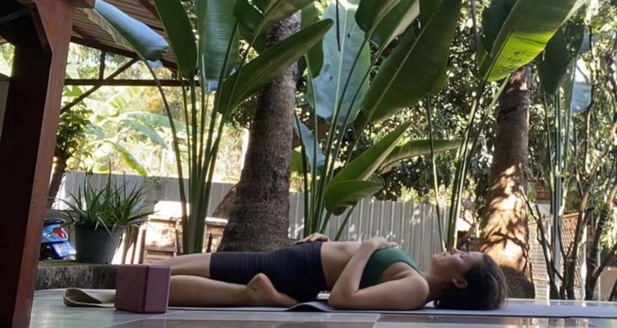 woman in green bralette and black bike shorts lays on the ground in a yoga pose