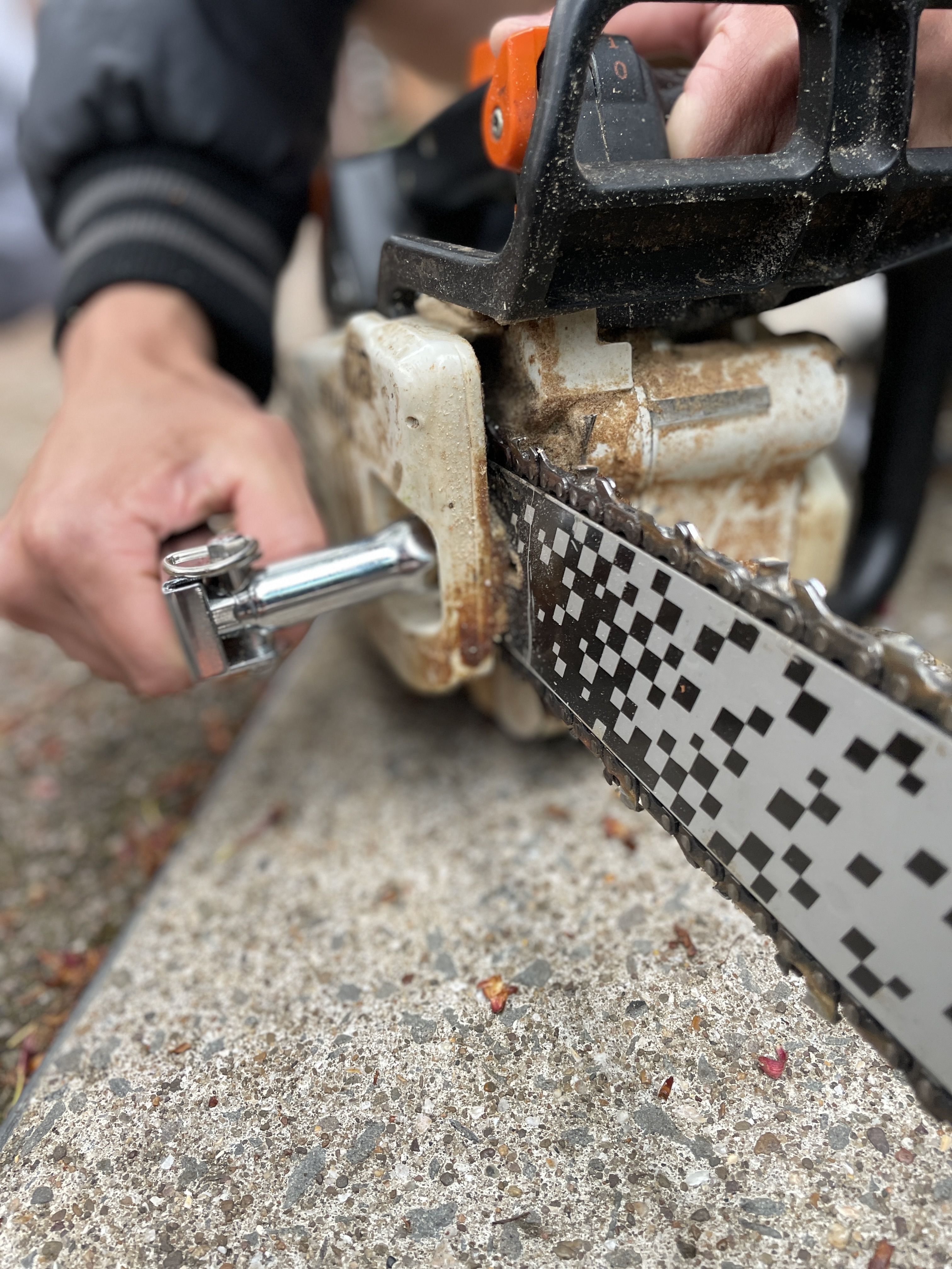 A person using a tool to adjust a chainsaw's blade.