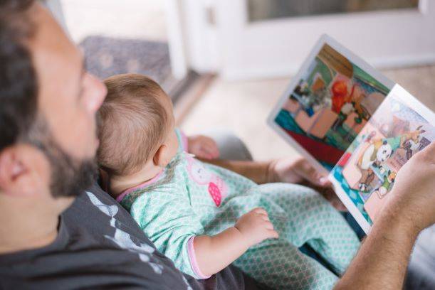Man Holding Baby Whilst Reading Book