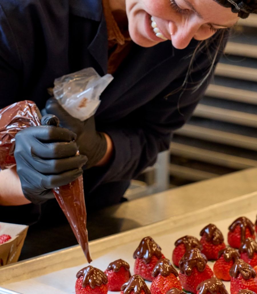Person decorating strawberries with chocolate in a kitchen setting.