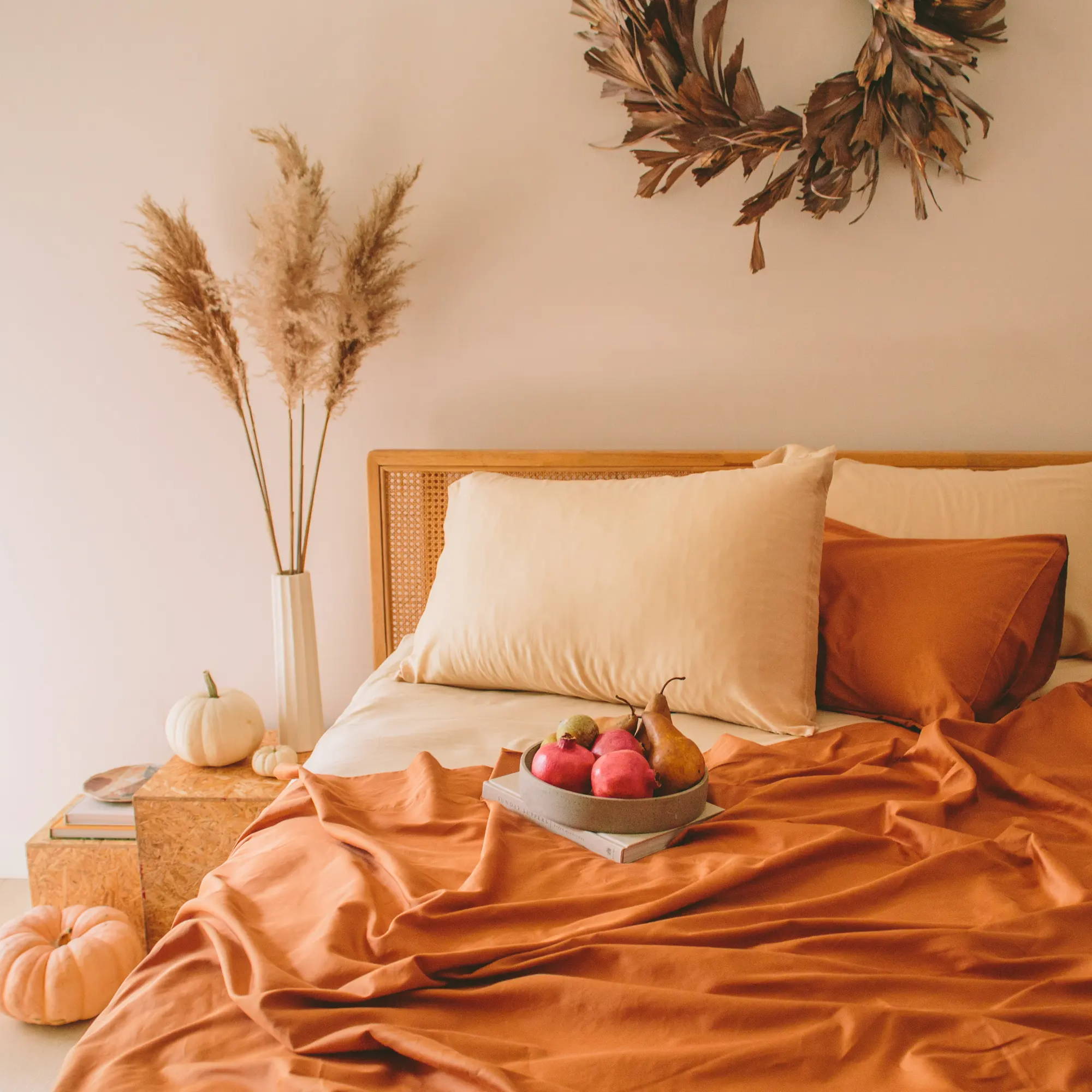 a beautiful boho bedrooms scene with pumpkins and fall fruits. The bed is made with a combination the nest bedding terracotta sateen organic cotton sheets and biscotti tencel sheets.