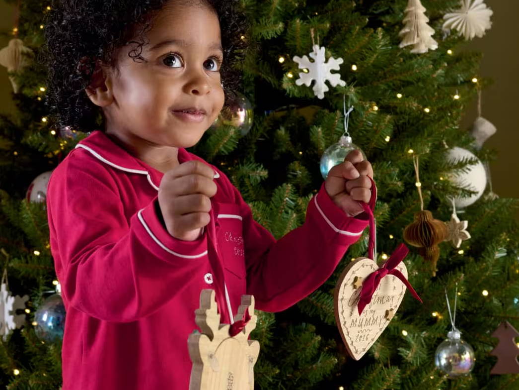 Child in red pajamas holding ornaments by a decorated Christmas tree.