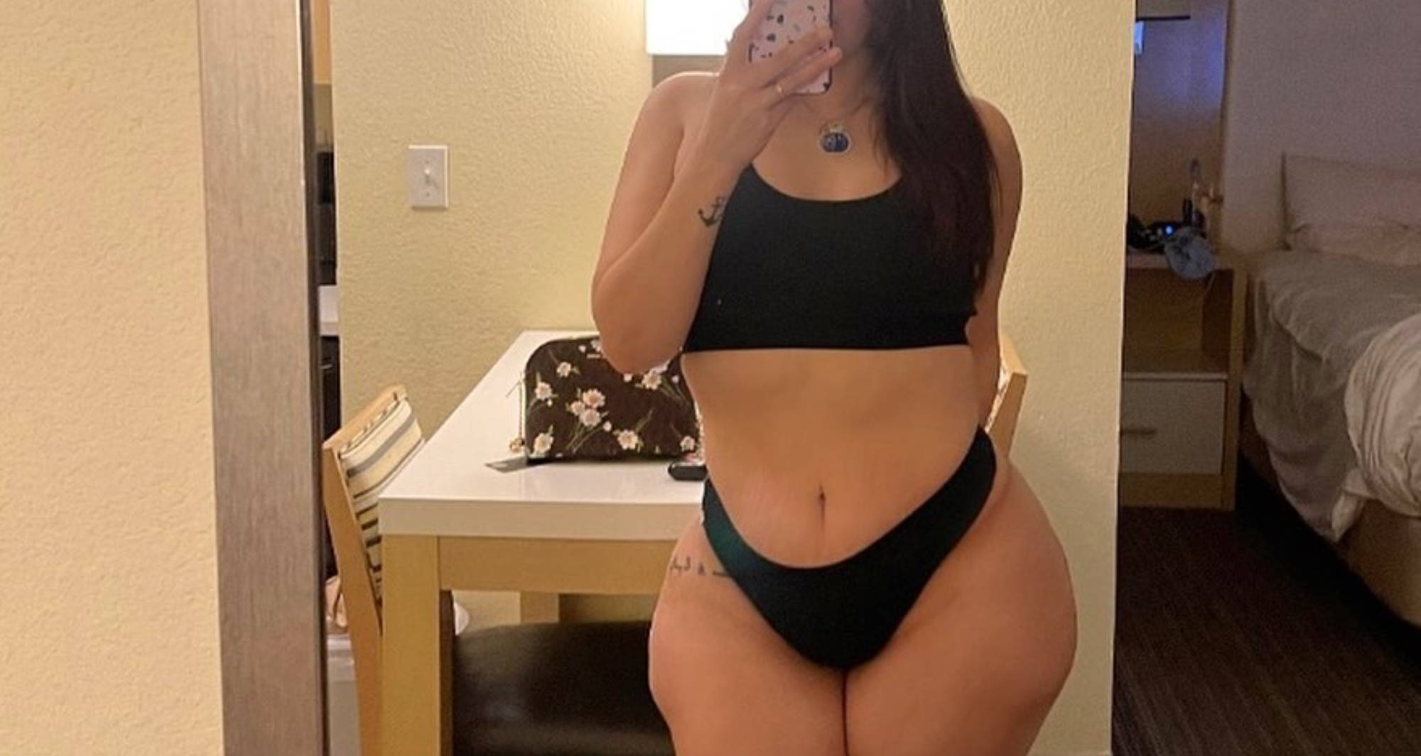  curvy woman takes a mirror selfie while wearing a black bralette and underwear set