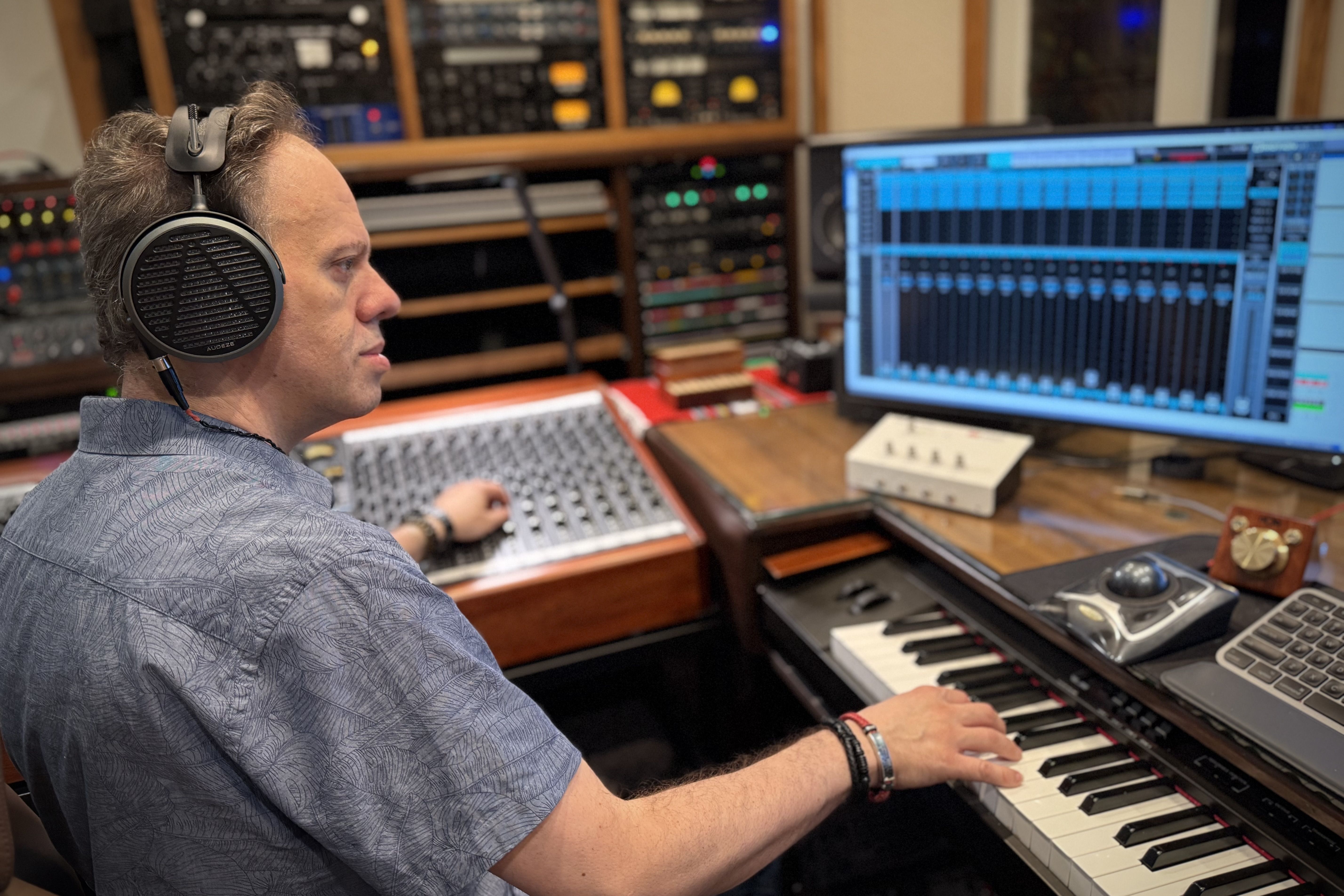 Person working in a music studio, using a keyboard and computer.