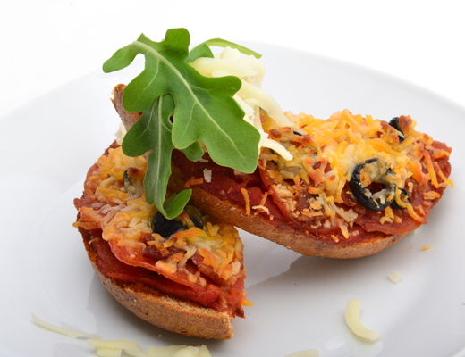 Two bagel halves topped with cheese, olives, and arugula on a plate.
