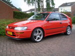 Front three-quarter Dennis's red 1995 Toyota Corolla hatchback silver wheels brick driveway Dutch plate Conductor's Special 232 train horn kit featured customer install gallery photo 1