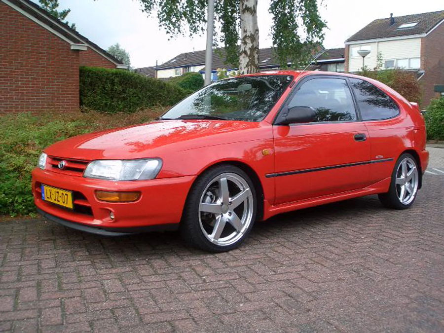 Front three-quarter Dennis's red 1995 Toyota Corolla hatchback silver wheels brick driveway Dutch plate Conductor's Special 232 train horn kit featured customer install gallery photo 1