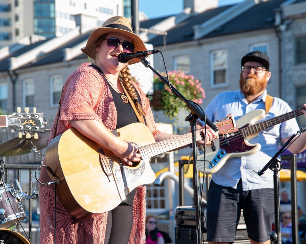 Musicians performing outdoors, one with an acoustic guitar, the other on bass.
