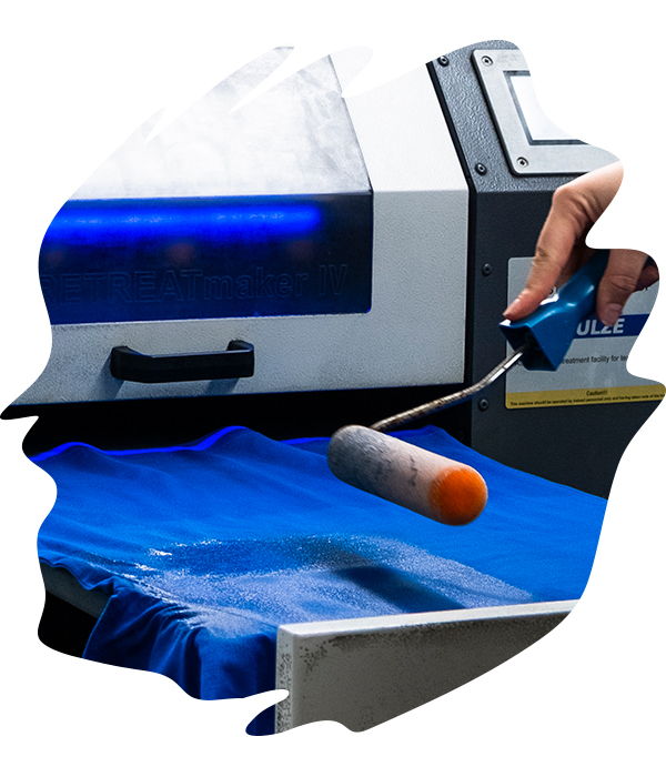 Close-up of garment being rollered with pre-treatment solution using industrial machine, preparing fabric for ink absorption.