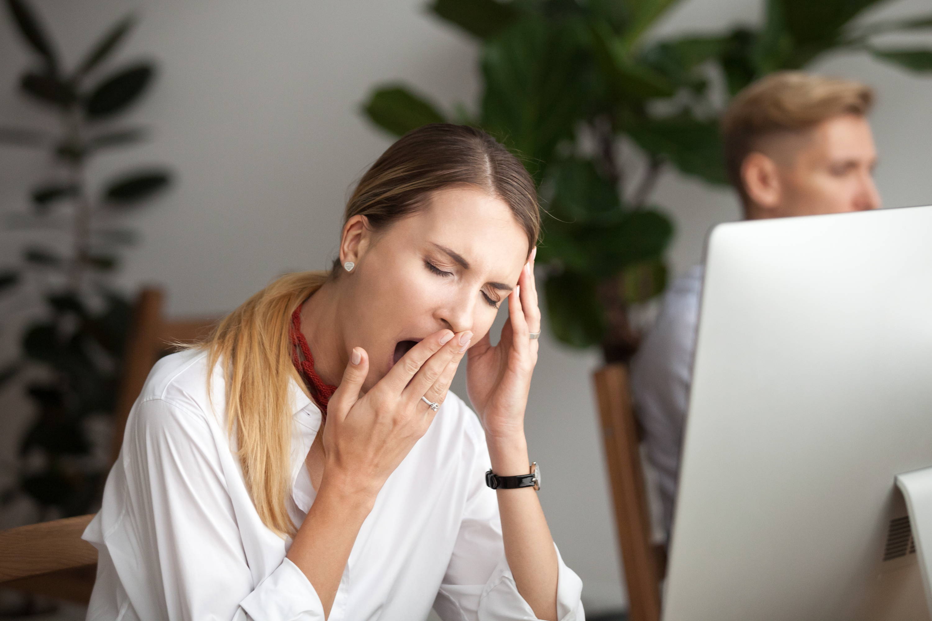 Young woman yawans by computer