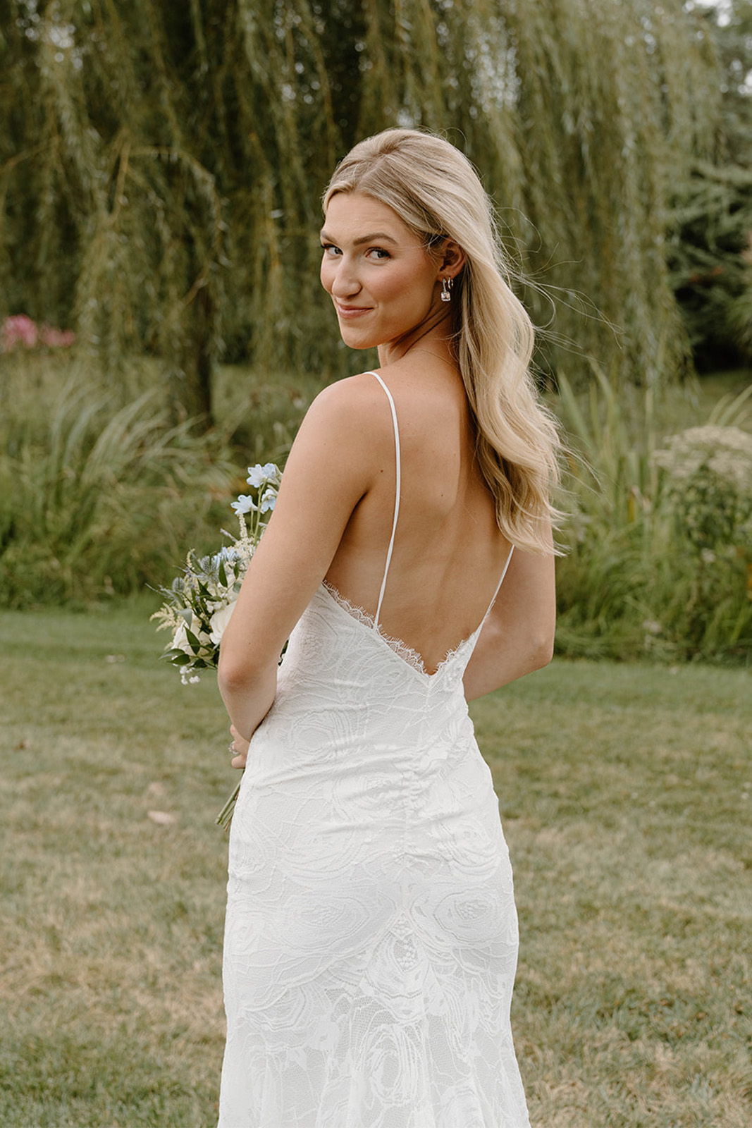 Bride in a white dress, smiling, holding a bouquet in a garden.