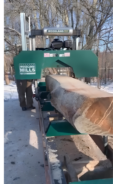 A sawmill processing a large log in a snowy environment.