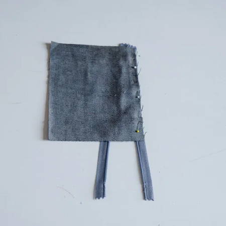A piece of denim fabric attached with pins to a zipper tape, ready to be stitched to the zipper