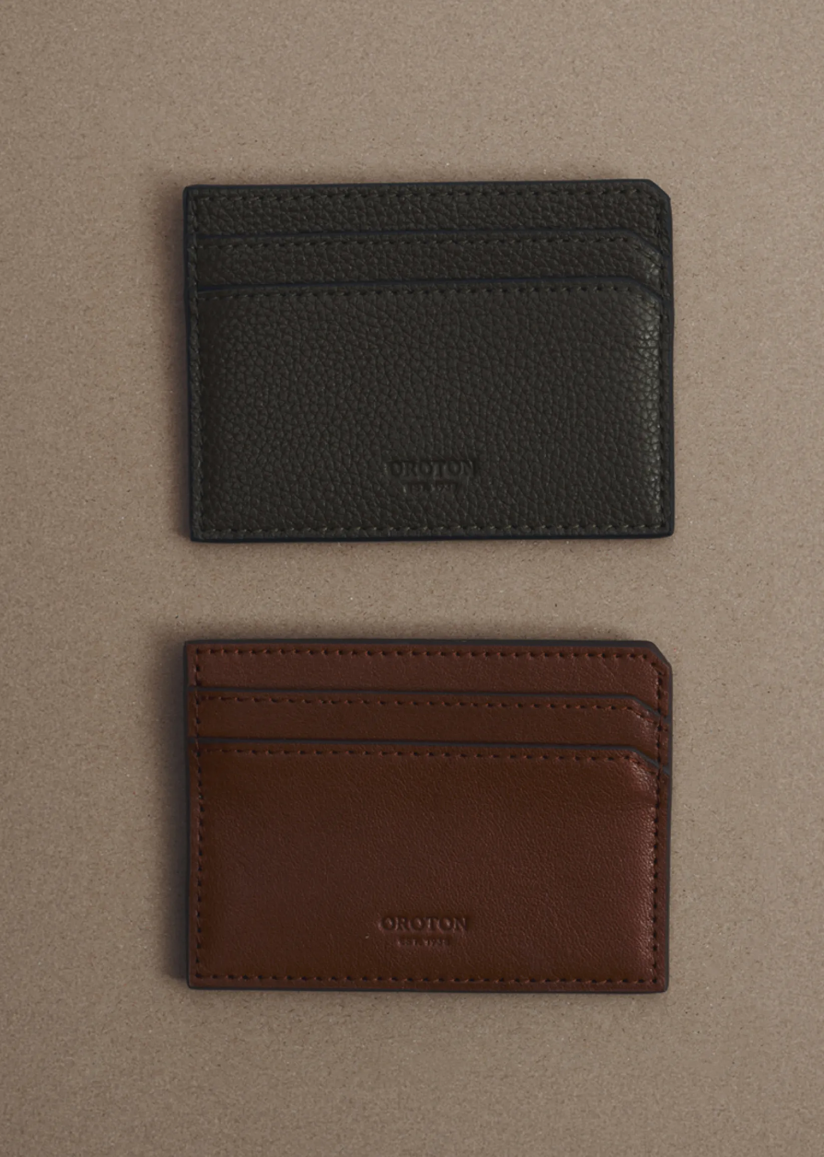Two leather cardholders, one dark gray and one brown, on a beige background.