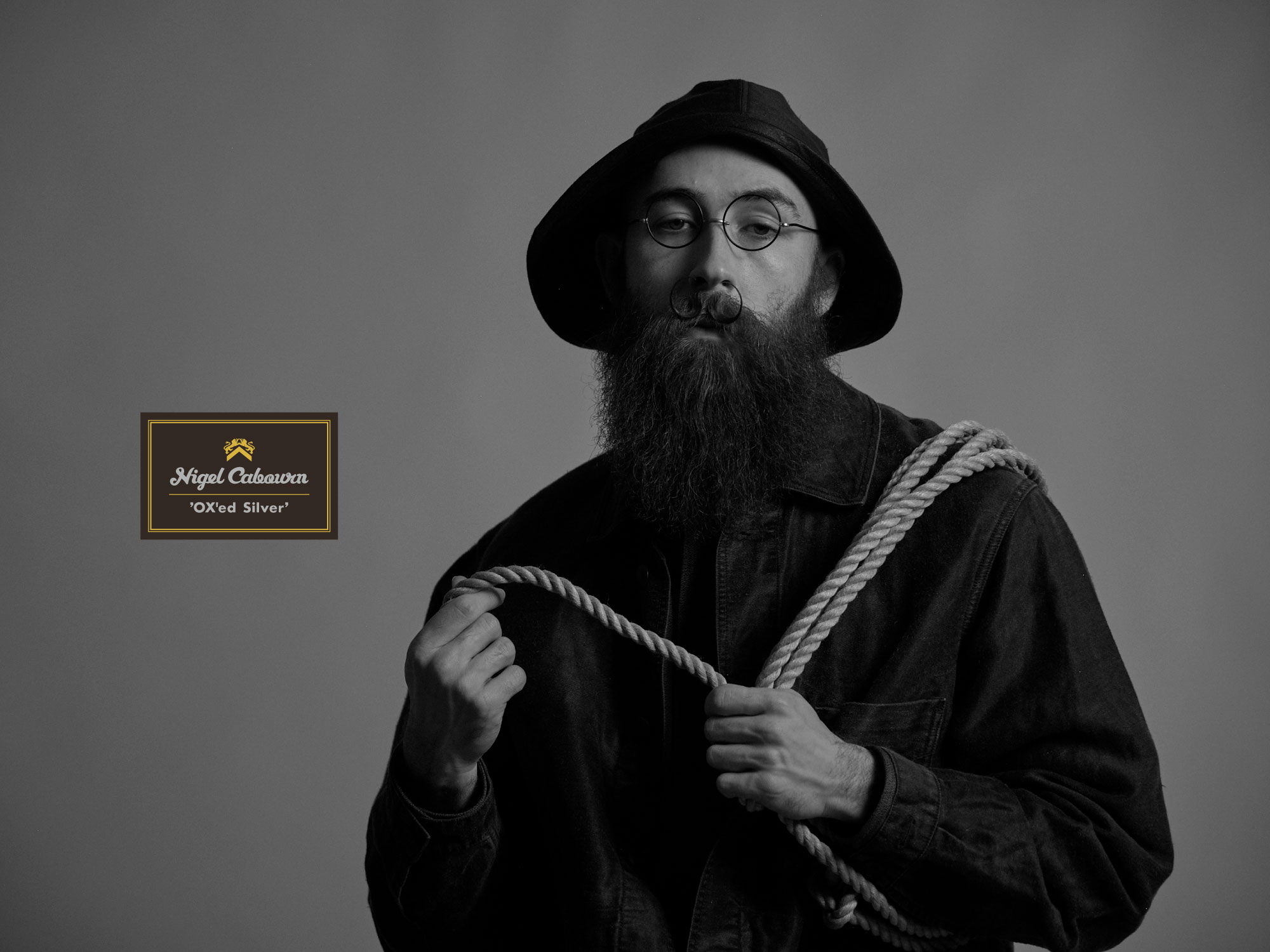 Man with a beard holding a rope, wearing a hat and coat.