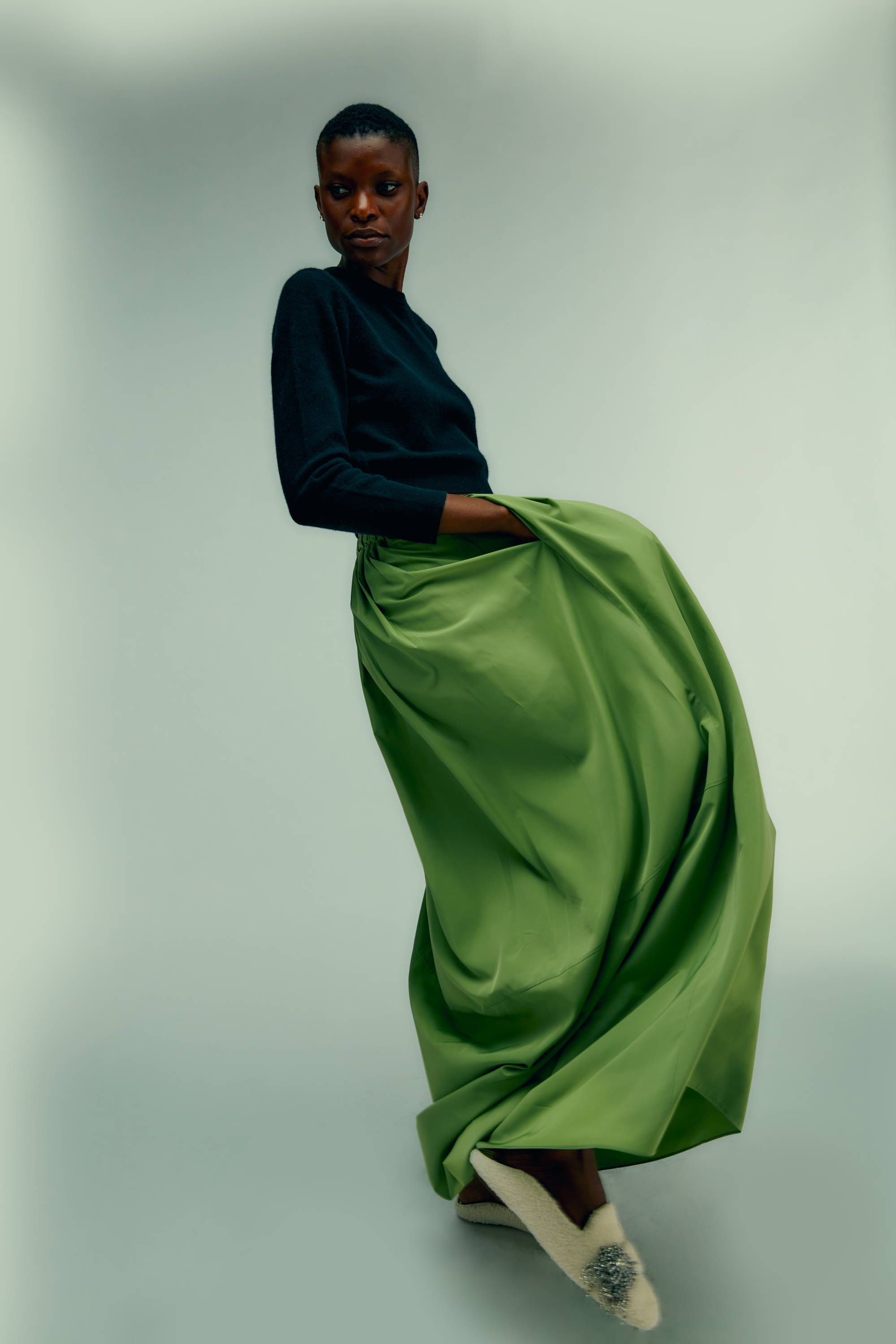 A model in a black top and green skirt poses elegantly.