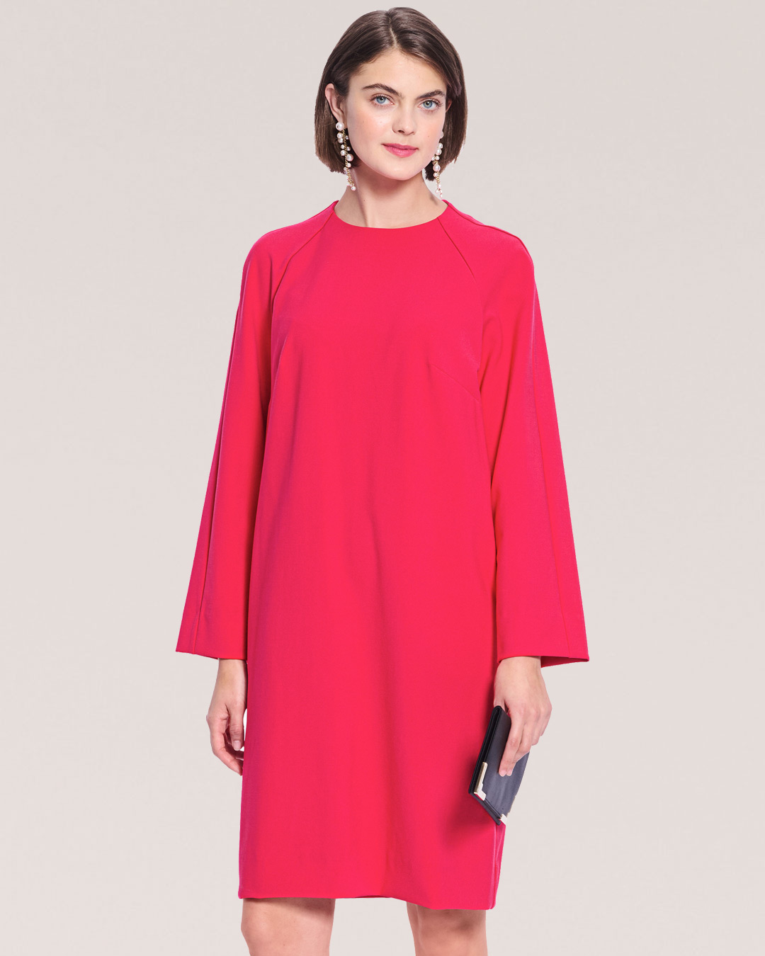 A woman in a pink dress holding a clutch.