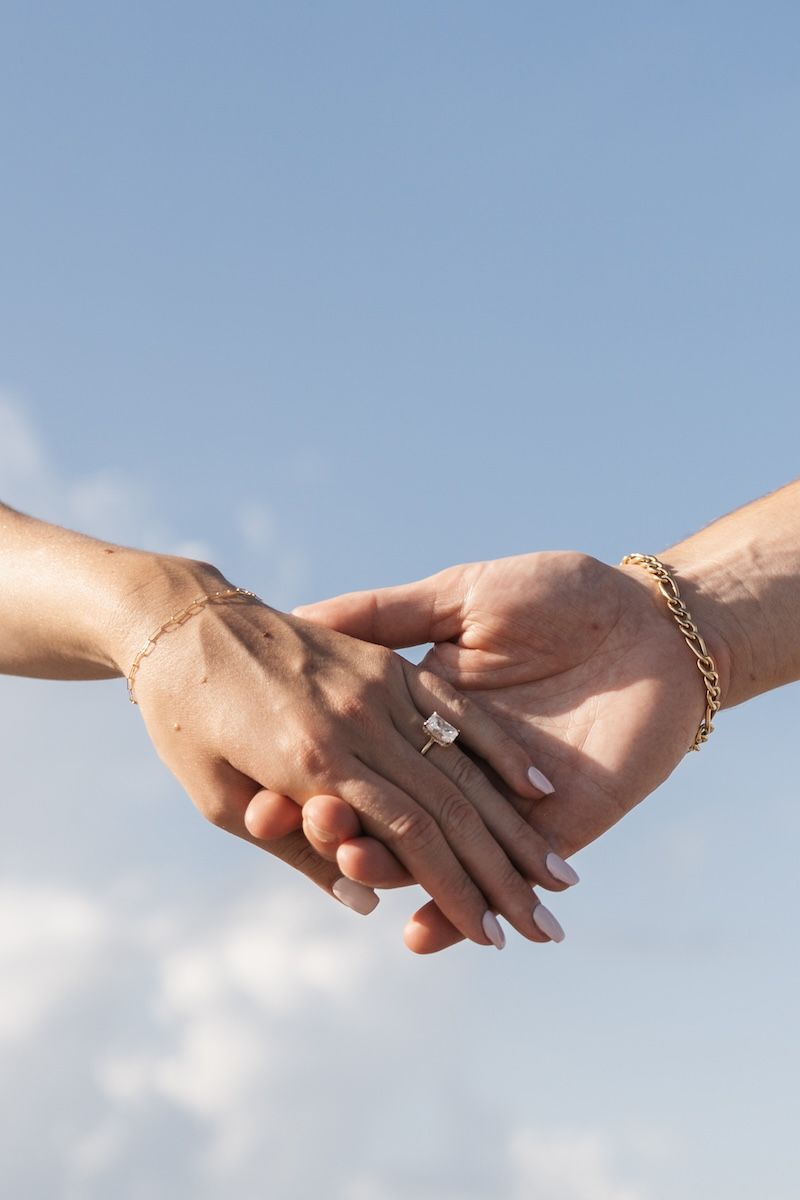 close up of holding hands and radiant cut engagement ring