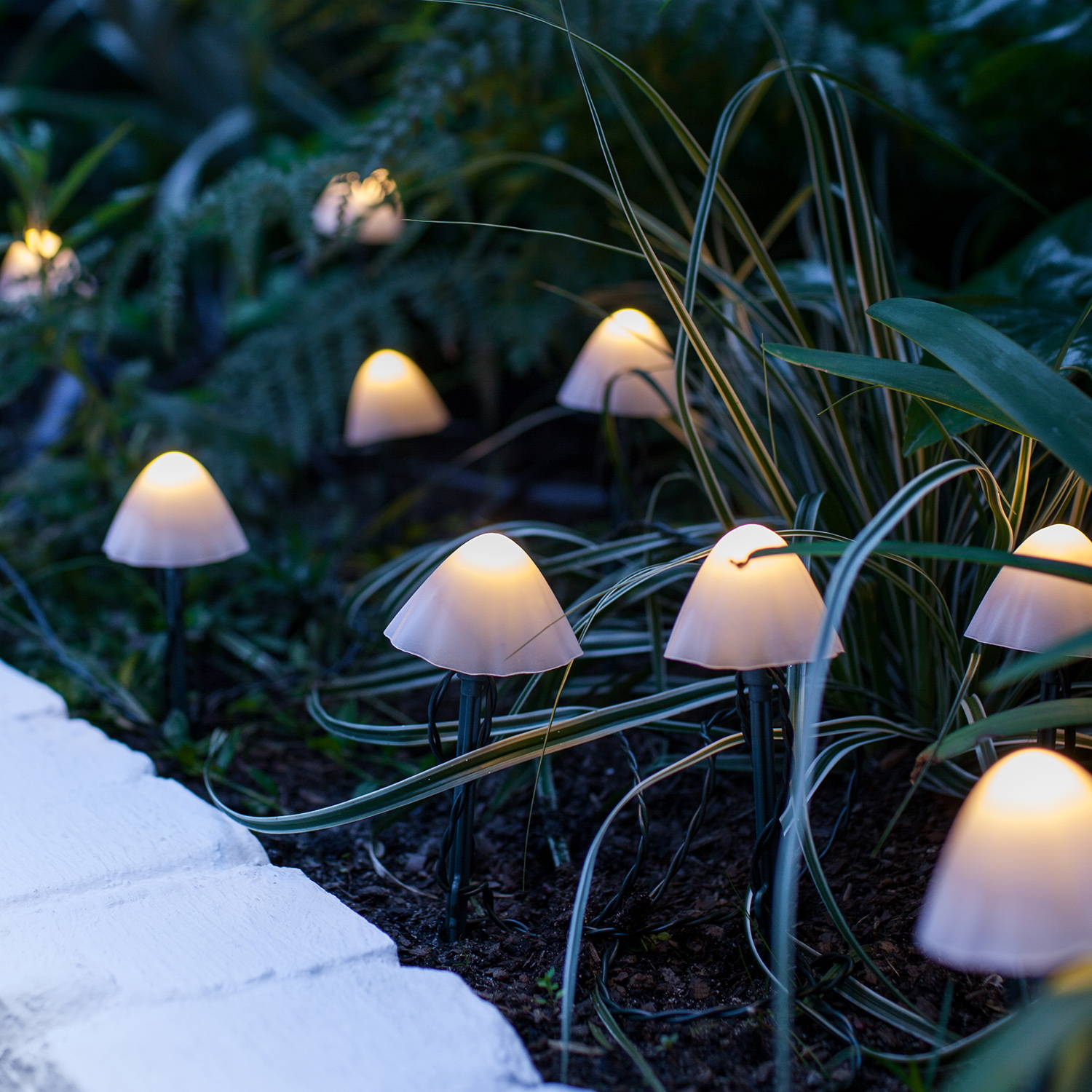 Mini white mushroom solar lights nestled in some grass in a garden.