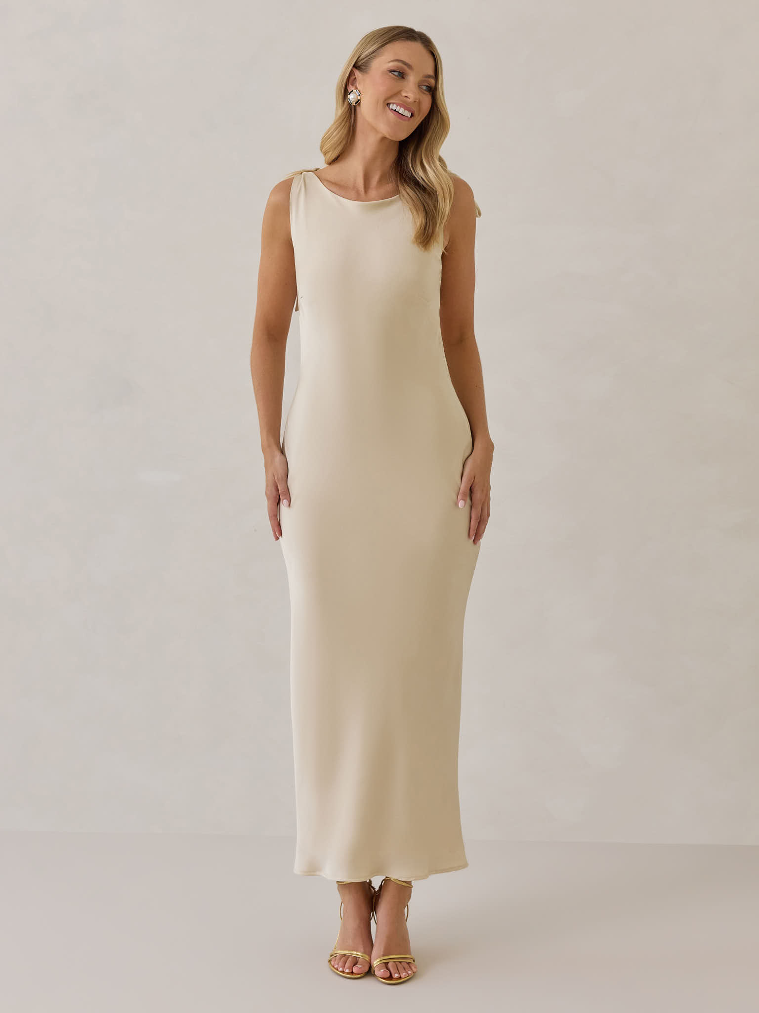 Woman in a backless beige dress with tied straps, standing gracefully.