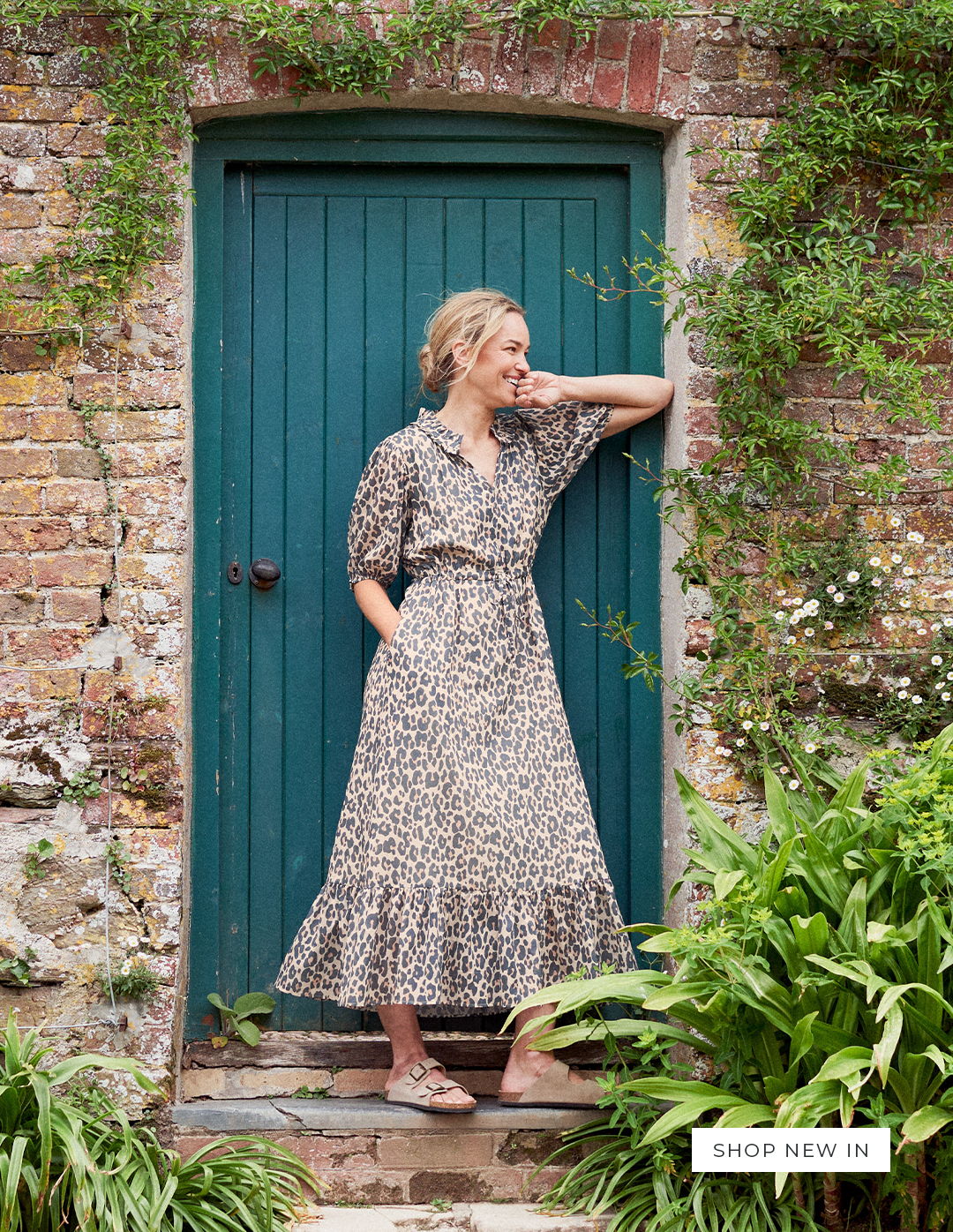 Woman standing in a doorway in a garden wearing a leopard print midi dress