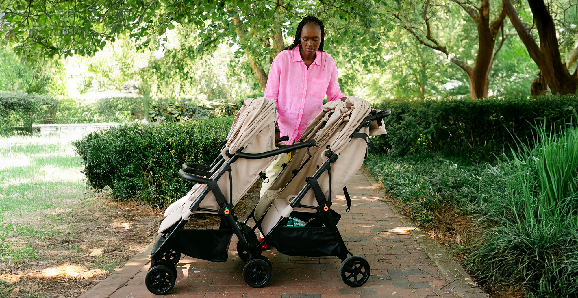 A person pushing a double stroller on a park path.