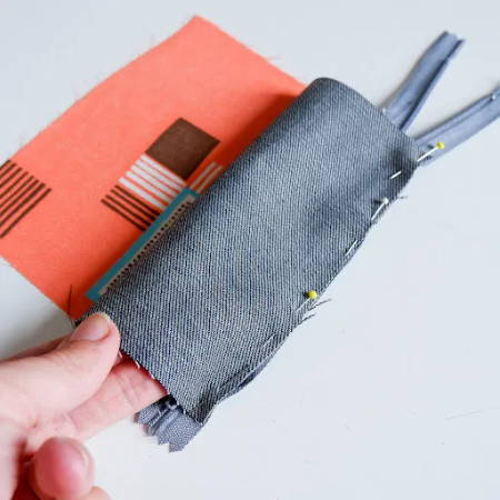 A piece of denim fabric attached with pins to the zipper tape to make a zippered pouch