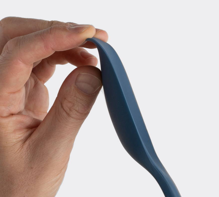 A hand bends the edge of a blue Misen Spoontula to demonstrate its flexibility.