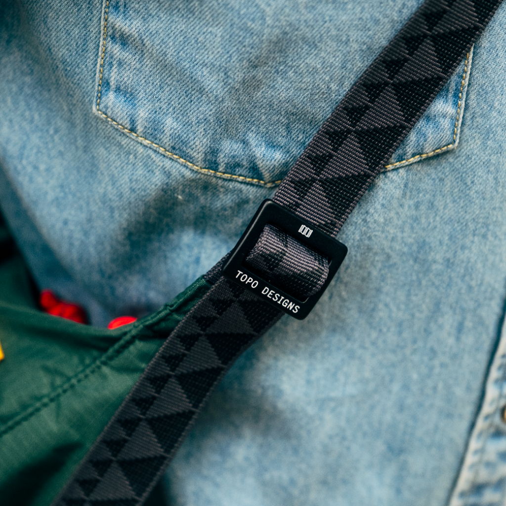 Close-up of a strap on denim with a green bag.