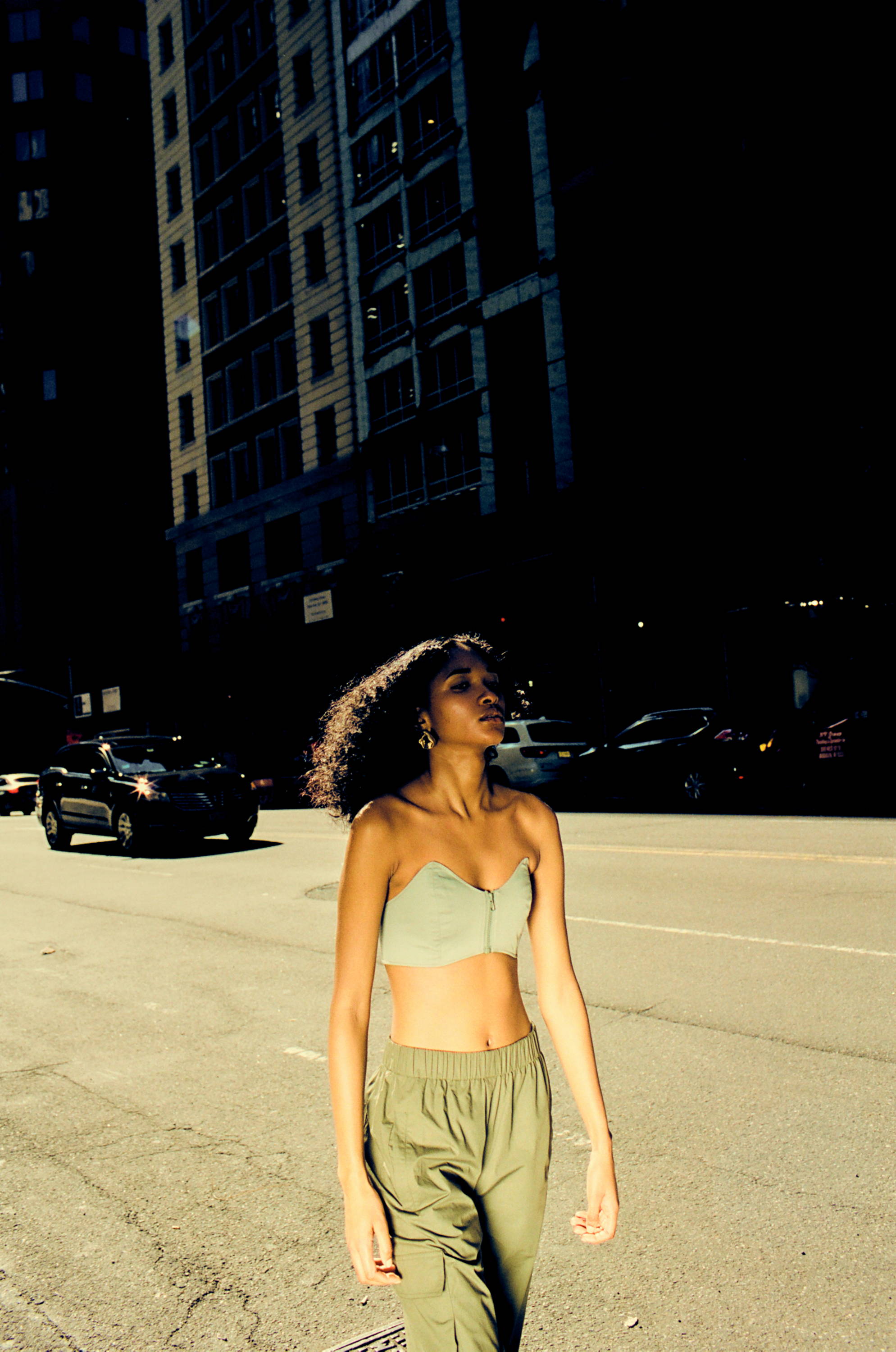 Person walking on a city street in casual clothing, sunlight illuminating the scene.