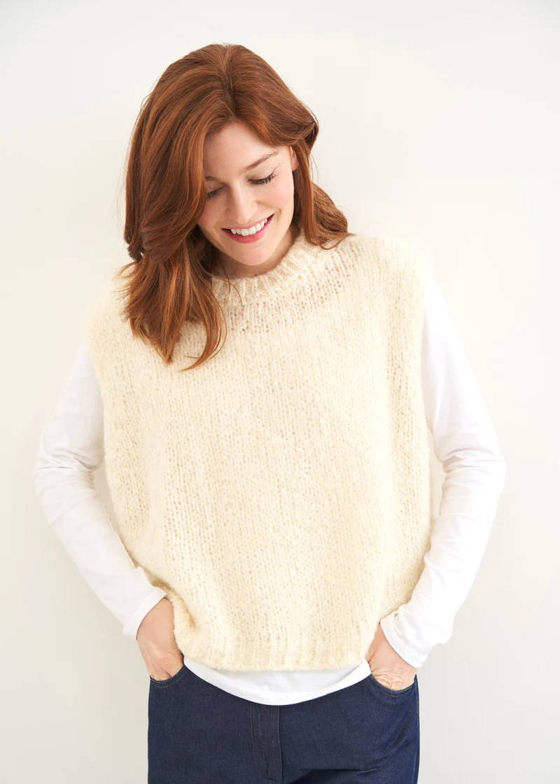 A model wearing a long sleeved white top with an off white sleevless knitted tank over the top