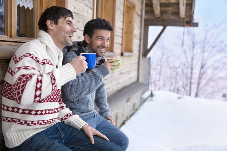 2 men sitting outside a winter cabin drinking from mugs