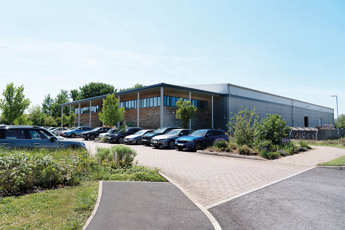 Modern building with parked cars and greenery under a clear blue sky.