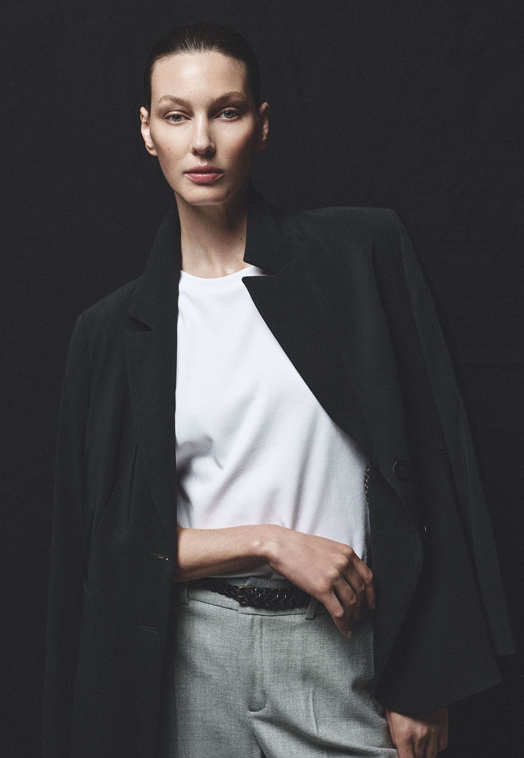 Model in a black coat and white shirt against a dark background.