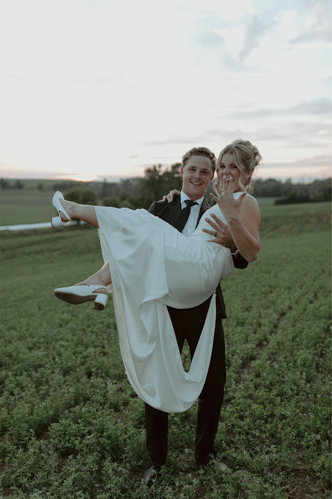 A couple celebrating, with the groom lifting the bride in a field.
