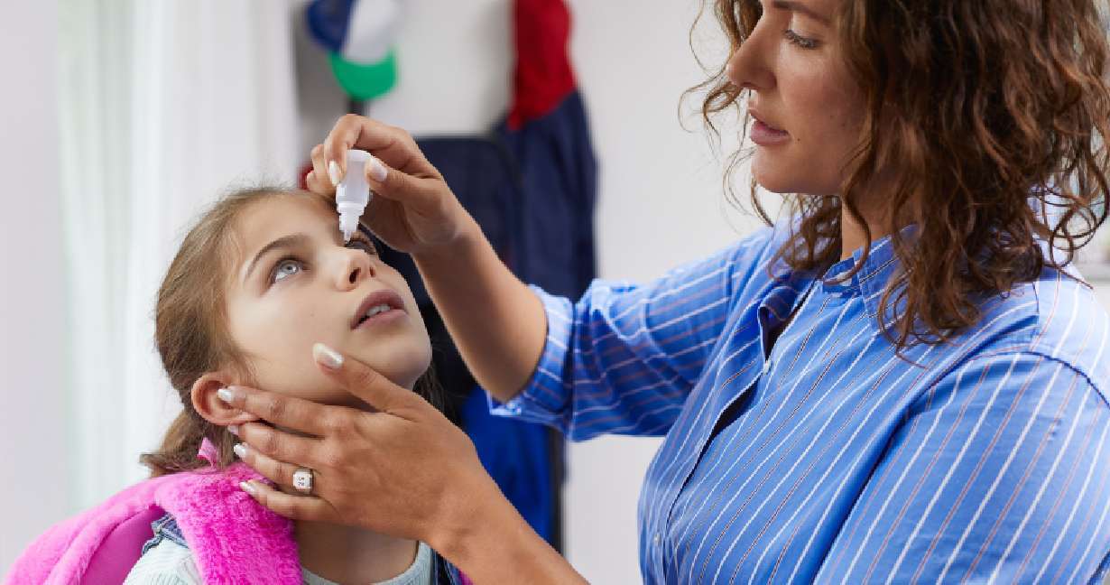 Maminka dává své dceři oční kapky před odchodem do školy – možná trpí alergií na pyl nebo roztoče domácího prachu.