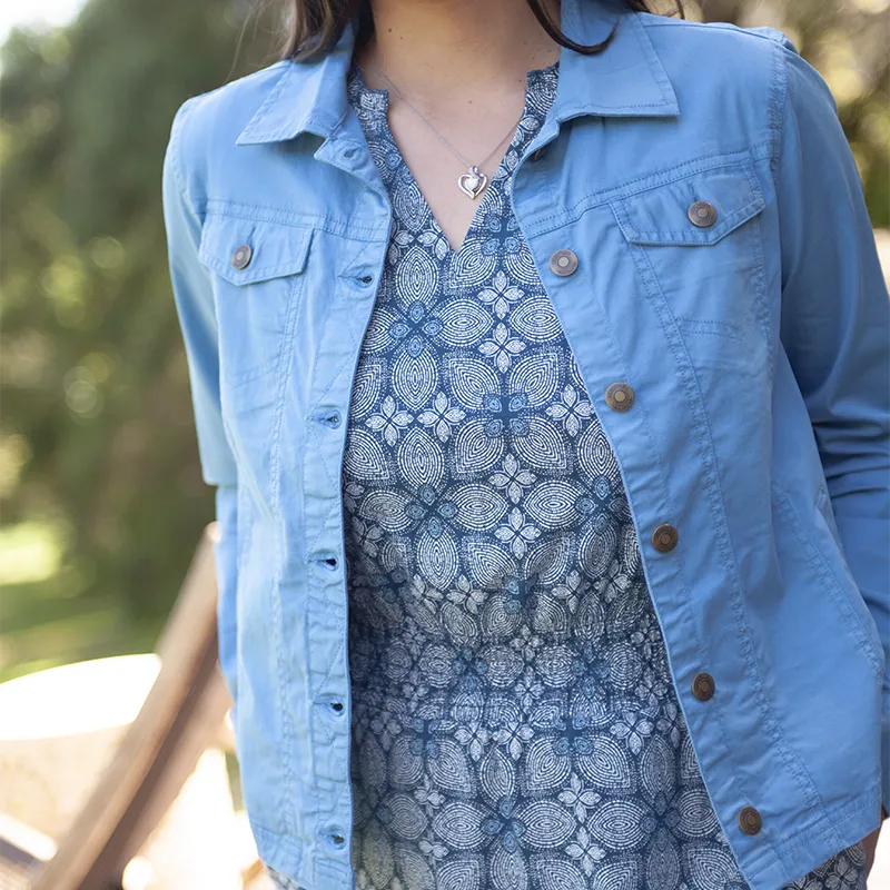 Person wearing a blue jacket over a patterned dress outdoors.