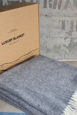 Gray luxury blanket next to its box on a concrete surface.