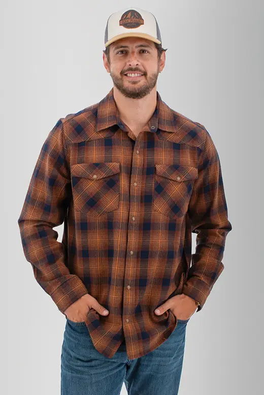 Man wearing a brown and blue plaid shirt with hands in pockets.